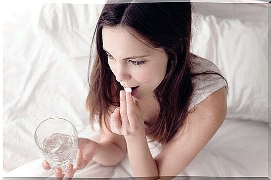 Woman in bed with glass of water taking medication